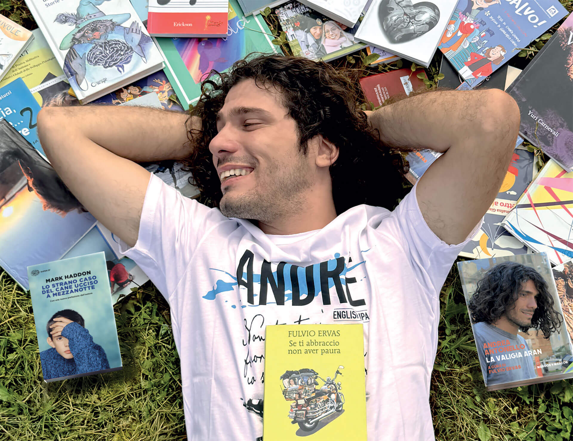 Andrea Antonello sdraiato sull'erba, sorridente con le mani dietro la testa, circondato da vari libri e riviste.